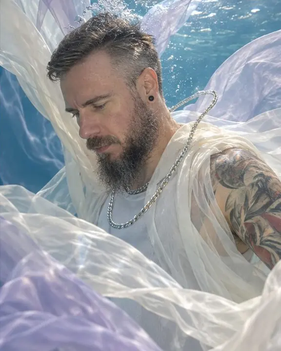 A floating silver chain and ivory organza against blue water lit by rippling caustic light