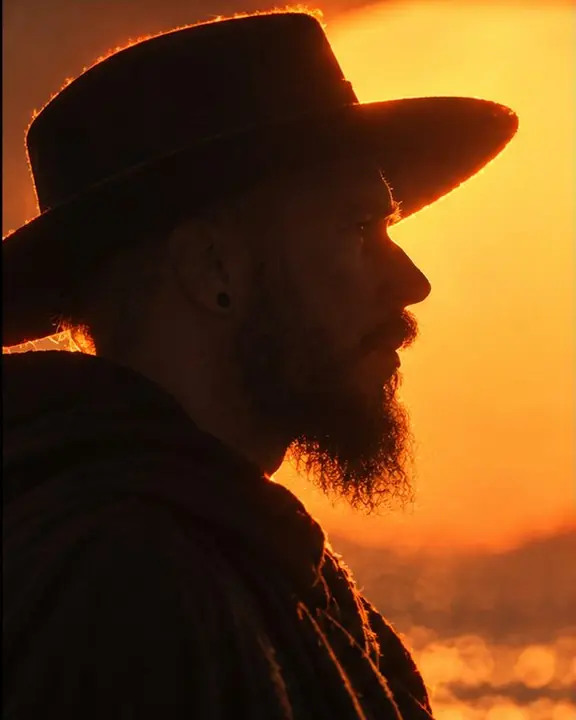 Profile silhouette of a bearded man in a sculptural hat cutting into the edge of a burning sun disc