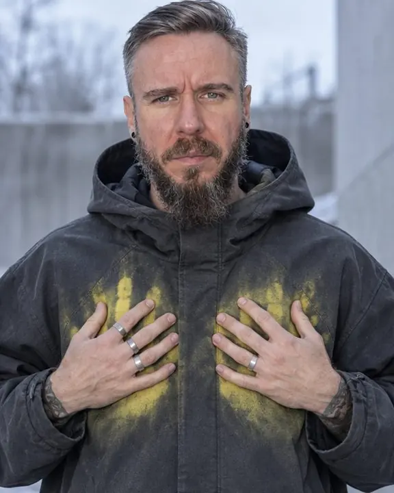 A man presses both palms flat to his graphite coat, bright yellow heat spreading out around his fingers