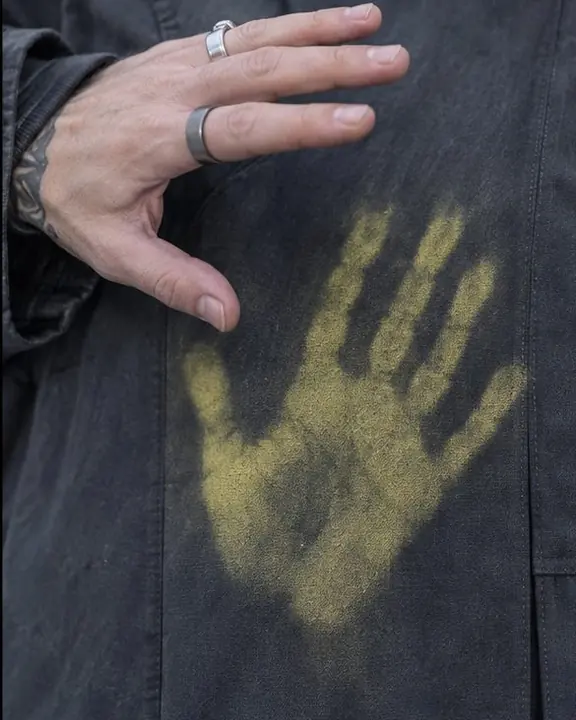 Close-up of a hand lifting off graphite fabric, leaving a bright acid-yellow handprint behind