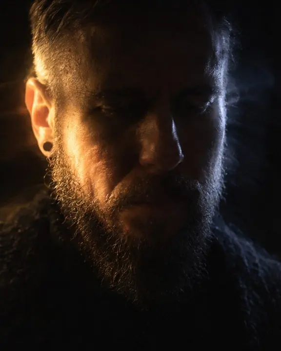 Close face of a bearded man with a warm patch of light on one cheek and a cold stroke on the other