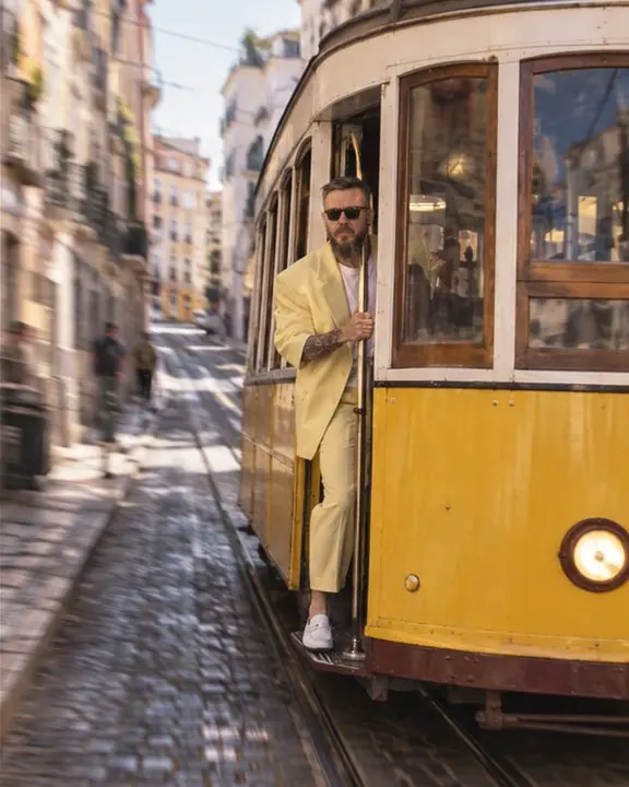 Front view of a yellow tram coming down a steep Lisbon street with a man in yellow standing at the door
