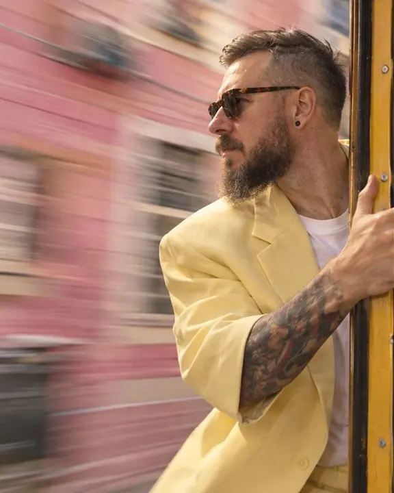 Profile of a bearded man in tortoiseshell sunglasses against pink walls streaked by a panning camera