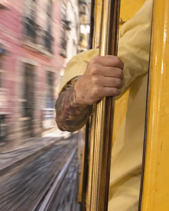 A hand gripping a brass pole against glossy yellow tram paint in warm afternoon sun