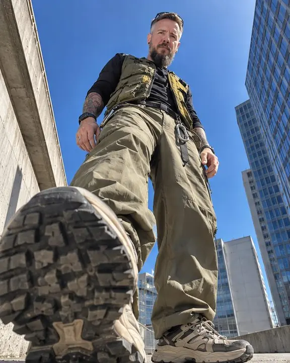 Worm's-eye view of a bearded man standing over the camera, one huge sneaker sole near the lens, buildings converging