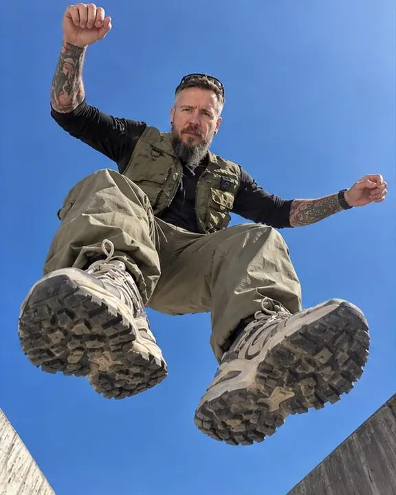 A man mid-jump against a deep blue sky seen from the ground, knees bent, both chunky sneakers large in the foreground
