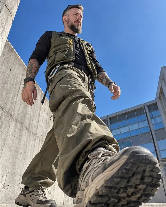 Low diagonal view as a man in khaki parachute pants walks past the lens, one leg and sneaker filling the corner
