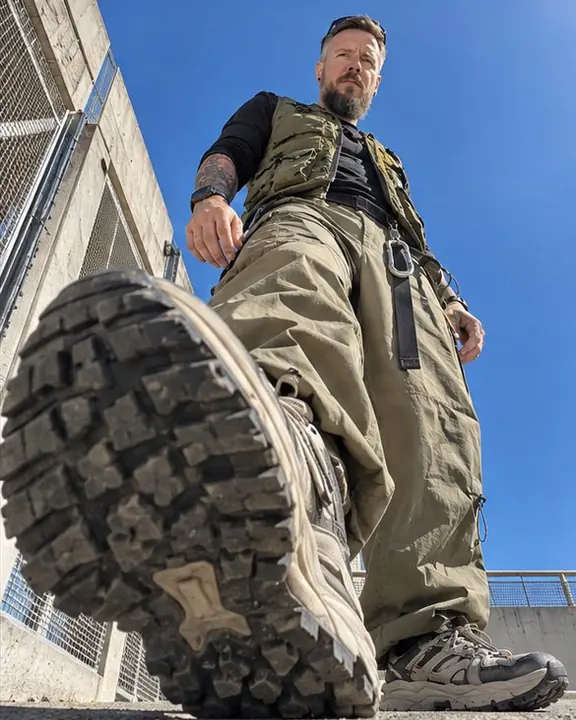 Ground-level close-up of lugged sneaker soles, a webbing belt and steel carabiner, a small face at the top