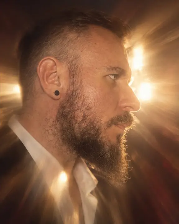 Profile of a bearded man, strong backlight smearing into long golden rays across his cheek