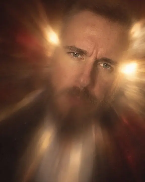 A man's face pushed off-center into a soft smear of gold light, only his eyes holding their shape