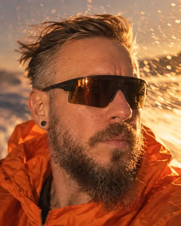 Close-up of a bearded man with wind in his hair, golden streaks of sea spray rushing past behind him
