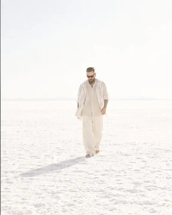 Wide view of a small figure in ecru clothes walking across white salt flats, the horizon nearly lost in glare