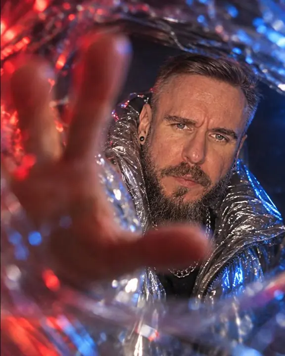 A man's hand reaching toward the lens as a smeared blur, his bearded face sharp behind it at night