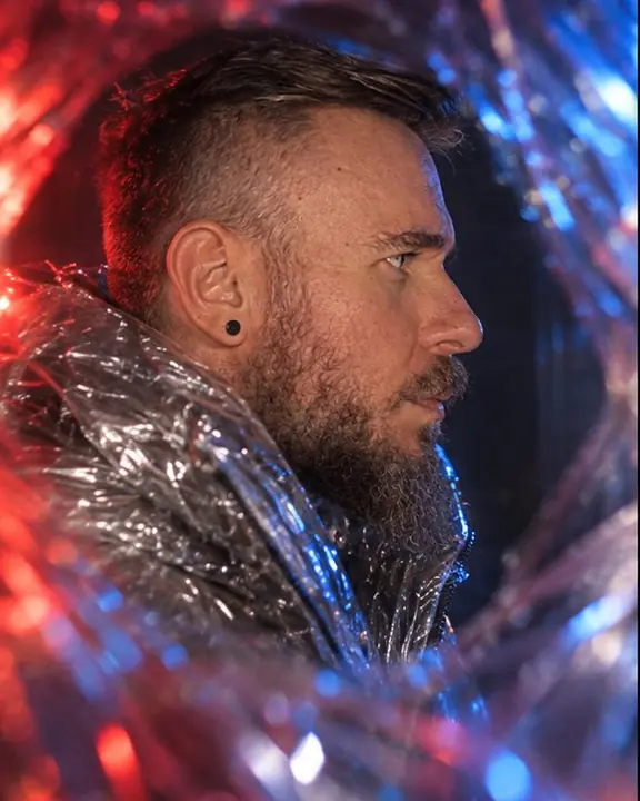 Profile of a bearded man drifting into a smeared edge of red and blue light from a film-wrapped lens