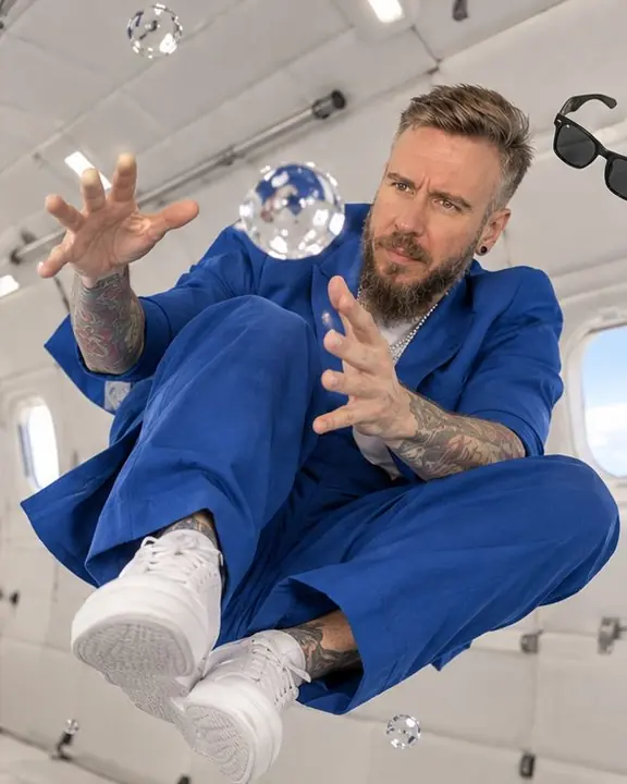 A man curls mid-spin with knees up in a blue suit, a floating sphere of water hanging in front of his face