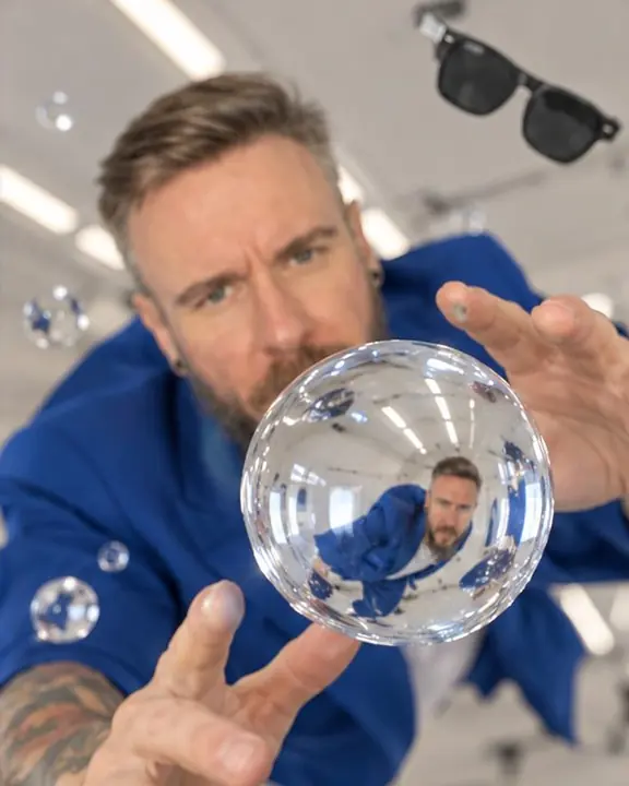A floating sphere of water hangs in midair, reflecting the electric blue of a suit in a white cabin