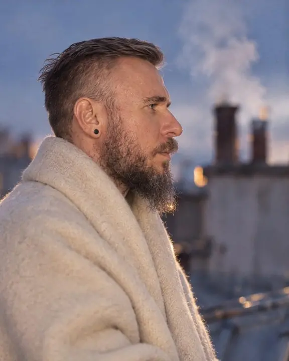 Profile of a bearded man against drifting chimney smoke over Paris roofs, soft blue-hour glow