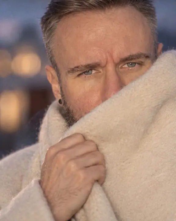 Close-up of a bearded man's eyes above cream cashmere, highlights blooming through a diffusion filter