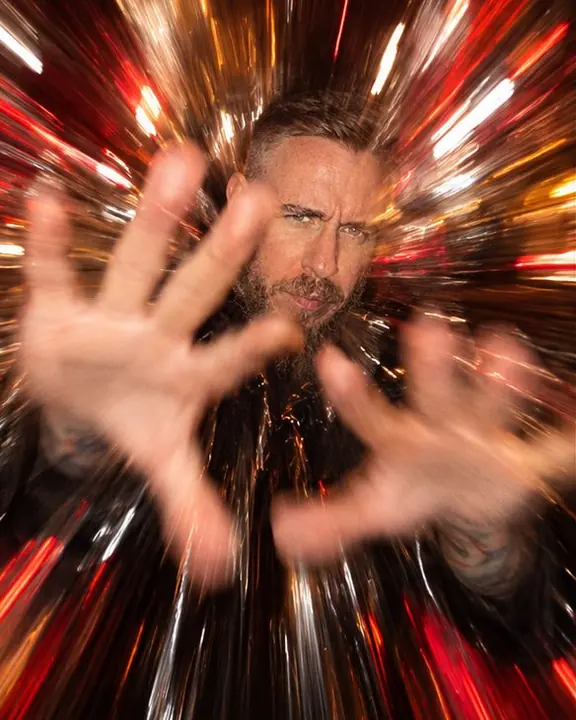 A man raises his hands toward the lens, stretched into lines of light, his face behind partly sharp